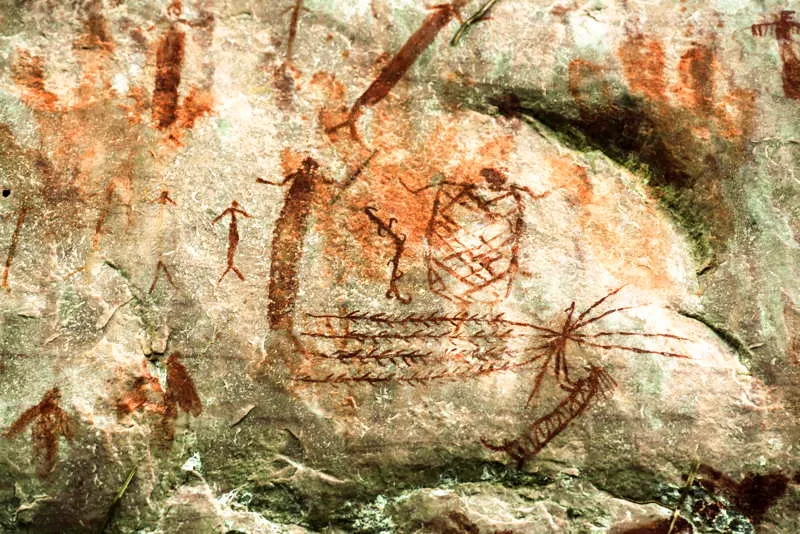 Una escena de cazadores- guerreros al lado de un chamn con atuendo ritual, que lleva en sus manos una sarta de venablos o lanzas con muescas o plumas. Las restantes figuras danzan en agitacin. 