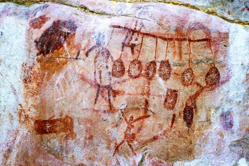 Hombres danzan con armas y sin ellas, al lado de una vara con mochilas o paneles de insectos, un cono muy emblemtico de Chiribiquete. 