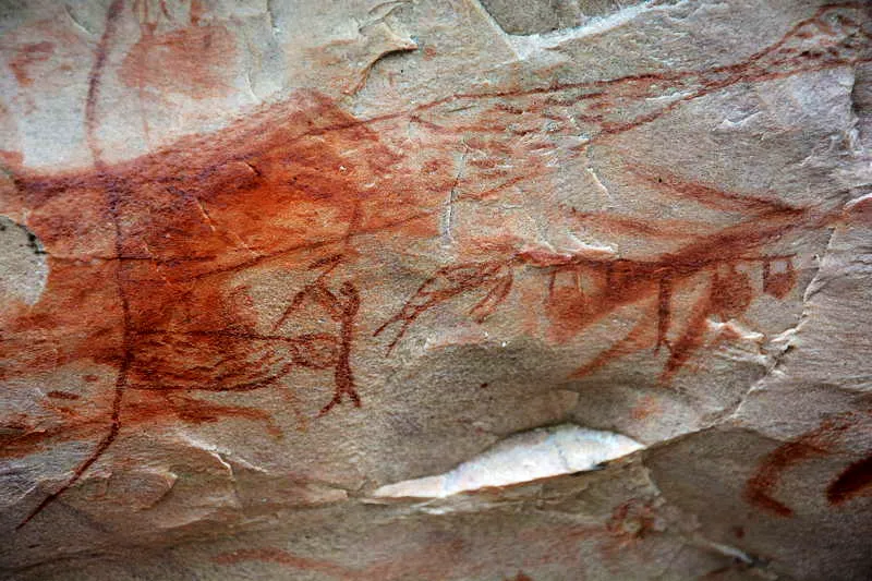 Varios cazadores, al lado de grandes redes para la captura de peces, observan el fluido de vida de estas nasas de donde salen/entran peces y hombrecitos. Un hombre con vara en sus hombros lleva varias mochilas cargadas con el vital alimento. Un jaguar y un venado acompaan la escena con gran predominancia. 