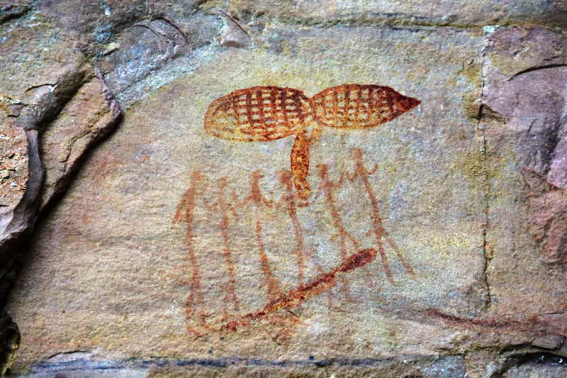 Un grupo de hombres baila encima de un poste-anaconda, con un par de cestas de captura de peces sobre sus cabezas. Un par de duendes regordetes acompaan la escena con varios peces piraa. 